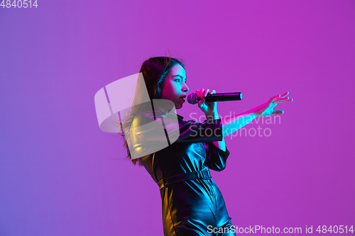 Image of Caucasian female singer portrait isolated on purple studio background in neon light