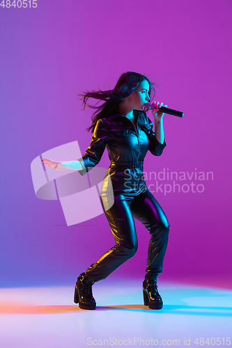 Image of Caucasian female singer portrait isolated on purple studio background in neon light