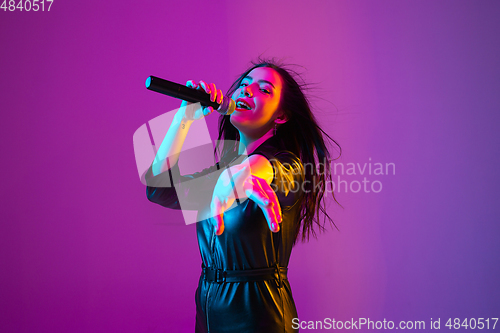 Image of Caucasian female singer portrait isolated on purple studio background in neon light