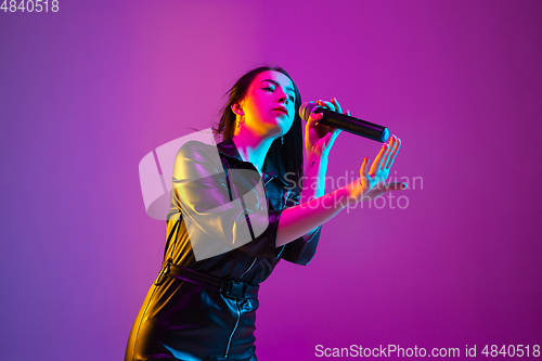 Image of Caucasian female singer portrait isolated on purple studio background in neon light