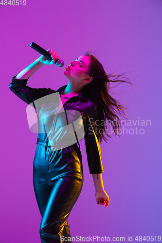 Image of Caucasian female singer portrait isolated on purple studio background in neon light