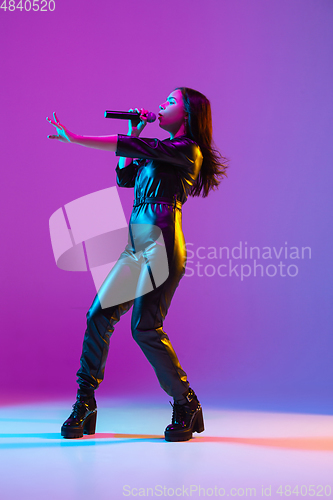 Image of Caucasian female singer portrait isolated on purple studio background in neon light