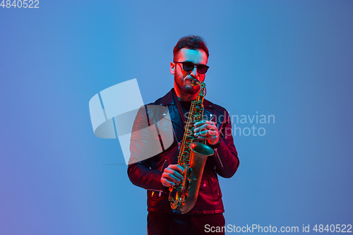 Image of Young caucasian jazz musician playing the saxophone in neon light