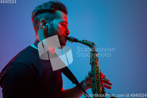 Image of Young caucasian jazz musician playing the saxophone in neon light