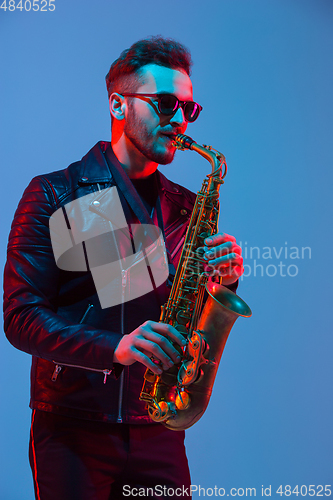 Image of Young caucasian jazz musician playing the saxophone in neon light