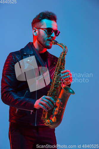 Image of Young caucasian jazz musician playing the saxophone in neon light