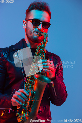 Image of Young caucasian jazz musician playing the saxophone in neon light