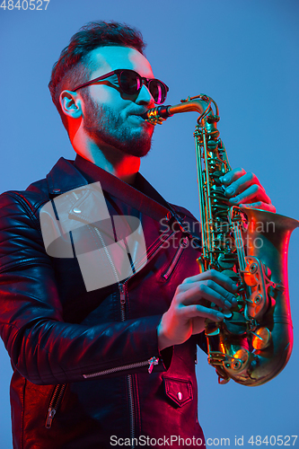Image of Young caucasian jazz musician playing the saxophone in neon light
