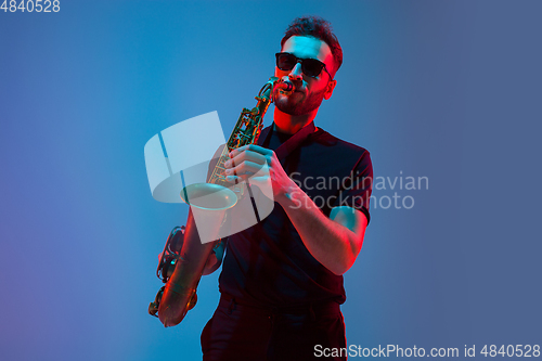 Image of Young caucasian jazz musician playing the saxophone in neon light