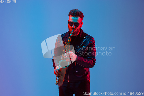 Image of Young caucasian jazz musician playing the saxophone in neon light