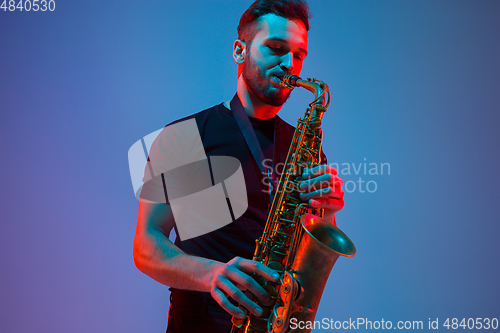 Image of Young caucasian jazz musician playing the saxophone in neon light