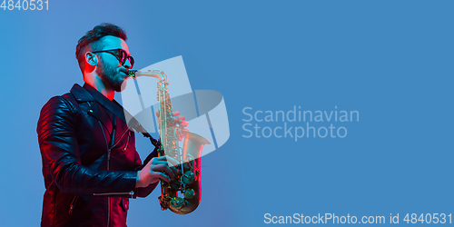 Image of Young caucasian jazz musician playing the saxophone in neon light, flyer