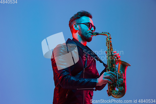 Image of Young caucasian jazz musician playing the saxophone in neon light