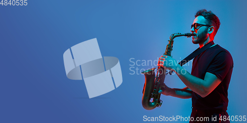 Image of Young caucasian jazz musician playing the saxophone in neon light, flyer