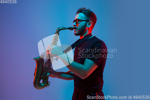 Image of Young caucasian jazz musician playing the saxophone in neon light