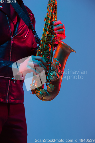 Image of Young caucasian jazz musician playing the saxophone in neon light, close up