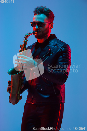 Image of Young caucasian jazz musician playing the saxophone in neon light