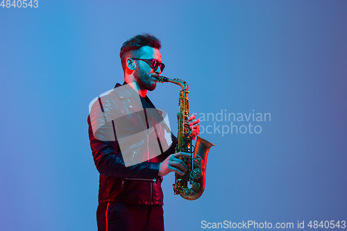 Image of Young caucasian jazz musician playing the saxophone in neon light