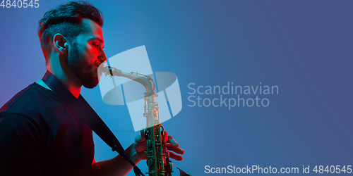 Image of Young caucasian jazz musician playing the saxophone in neon light, flyer