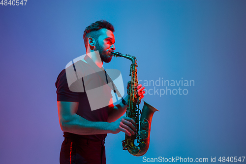 Image of Young caucasian jazz musician playing the saxophone in neon light