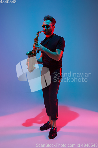 Image of Young caucasian jazz musician playing the saxophone in neon light