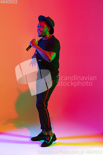 Image of Young african-american musician singing, dancing in neon light