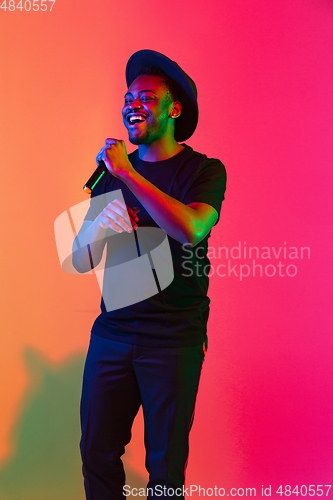 Image of Young african-american musician singing, dancing in neon light