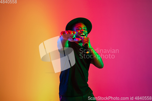 Image of Young african-american musician singing, dancing in neon light