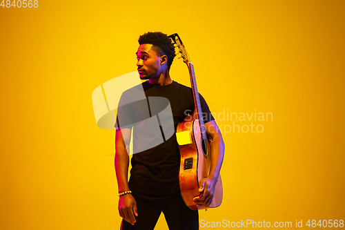 Image of Young african-american musician singing, playing guitar in neon light