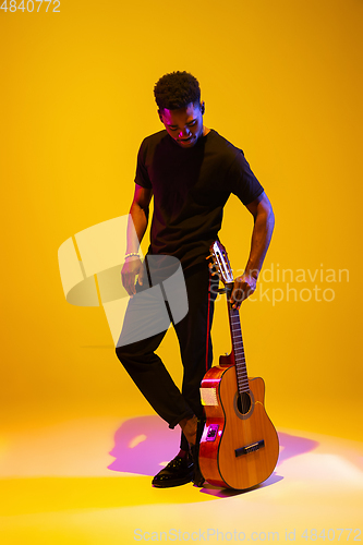 Image of Young african-american musician singing, playing guitar in neon light