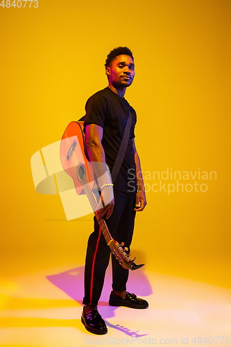 Image of Young african-american musician singing, playing guitar in neon light