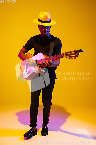 Image of Young african-american musician singing, playing guitar in neon light