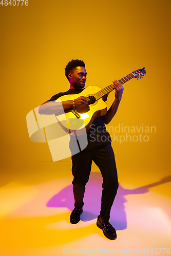 Image of Young african-american musician singing, playing guitar in neon light