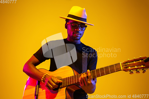 Image of Young african-american musician singing, playing guitar in neon light