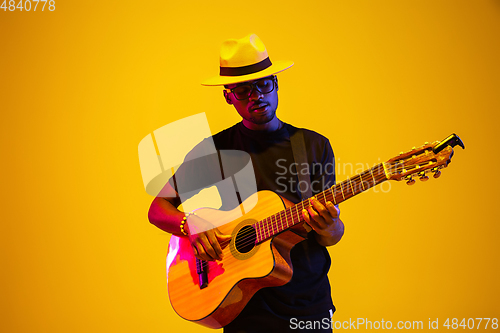 Image of Young african-american musician singing, playing guitar in neon light