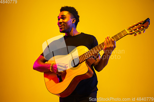 Image of Young african-american musician singing, playing guitar in neon light