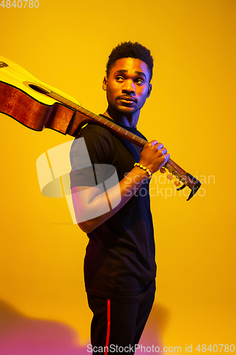 Image of Young african-american musician singing, playing guitar in neon light