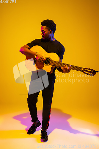 Image of Young african-american musician singing, playing guitar in neon light