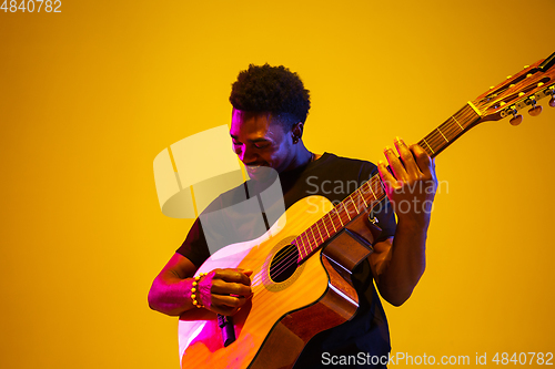 Image of Young african-american musician singing, playing guitar in neon light