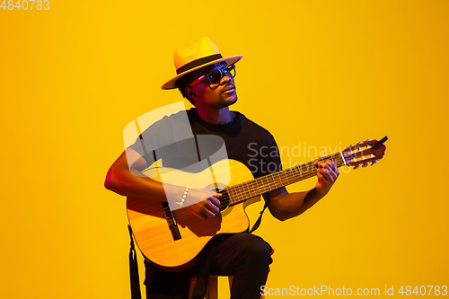 Image of Young african-american musician singing, playing guitar in neon light