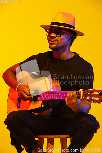 Image of Young african-american musician singing, playing guitar in neon light