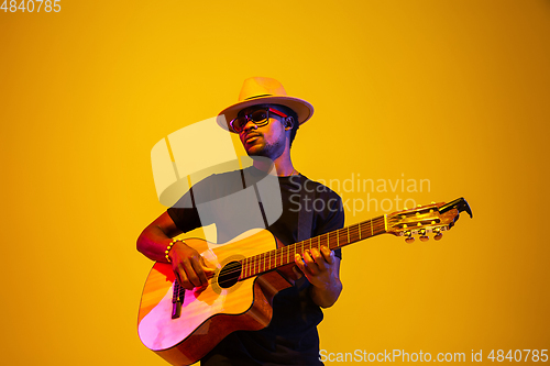 Image of Young african-american musician singing, playing guitar in neon light