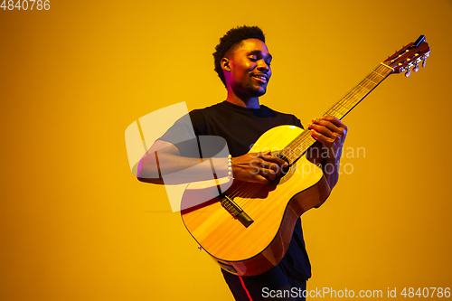 Image of Young african-american musician singing, playing guitar in neon light