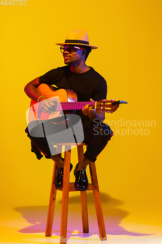 Image of Young african-american musician singing, playing guitar in neon light