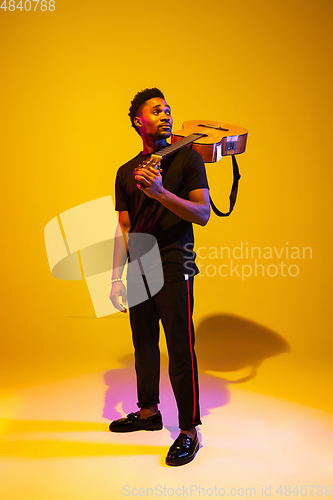 Image of Young african-american musician singing, playing guitar in neon light