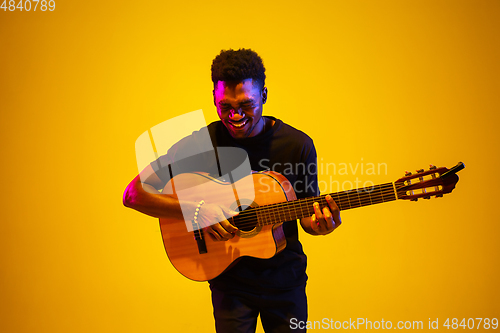 Image of Young african-american musician singing, playing guitar in neon light