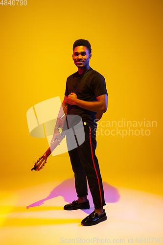 Image of Young african-american musician singing, playing guitar in neon light