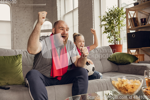Image of Excited, happy daughter and father watch football, soccer match together on the couch at home