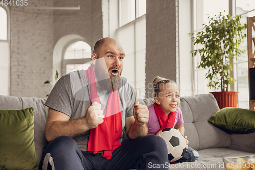 Image of Excited, happy daughter and father watch football, soccer match together on the couch at home