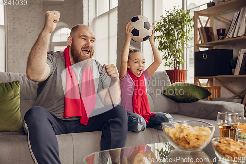 Image of Excited, happy daughter and father watch football, soccer match together on the couch at home